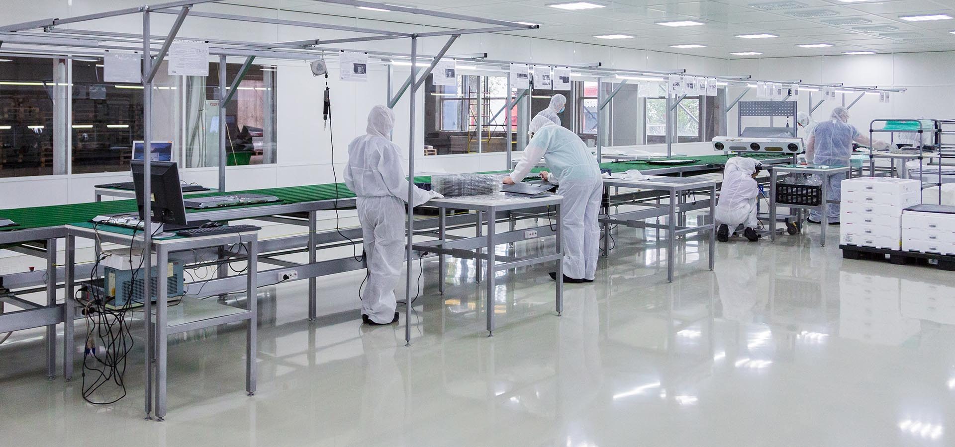 factory workers in white lab suits, producing tv sets on assebly line with some modern equipment in a clean room